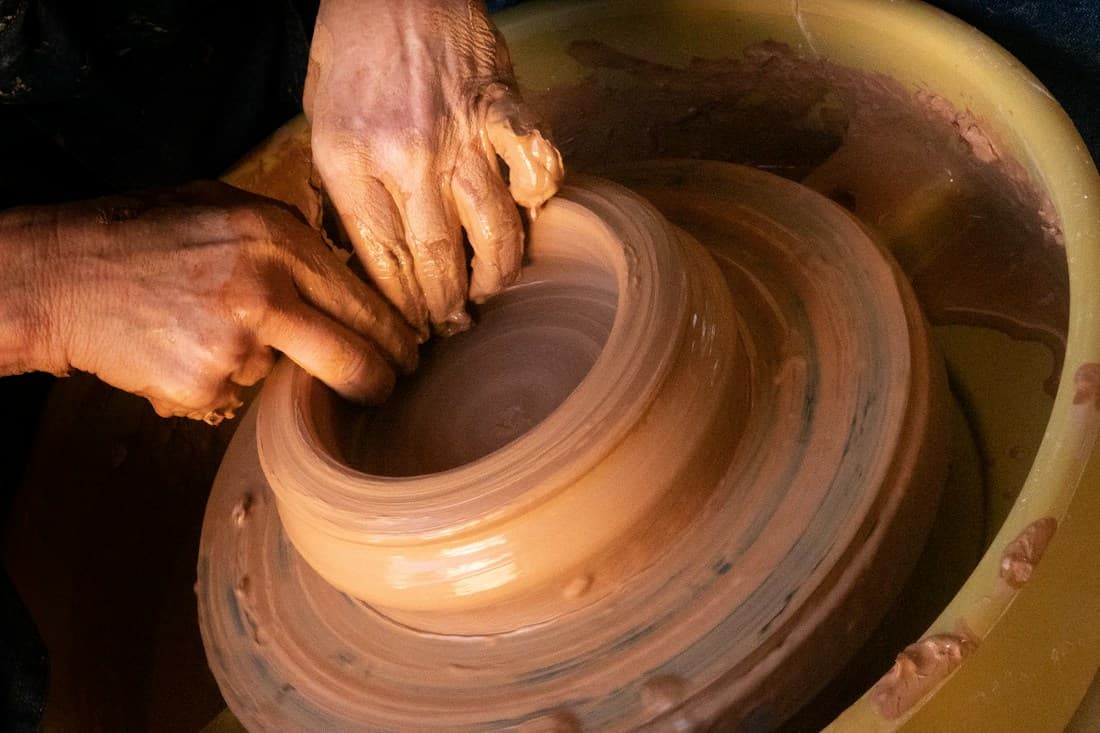 Hands shaping a clay vessel on a pottery wheel